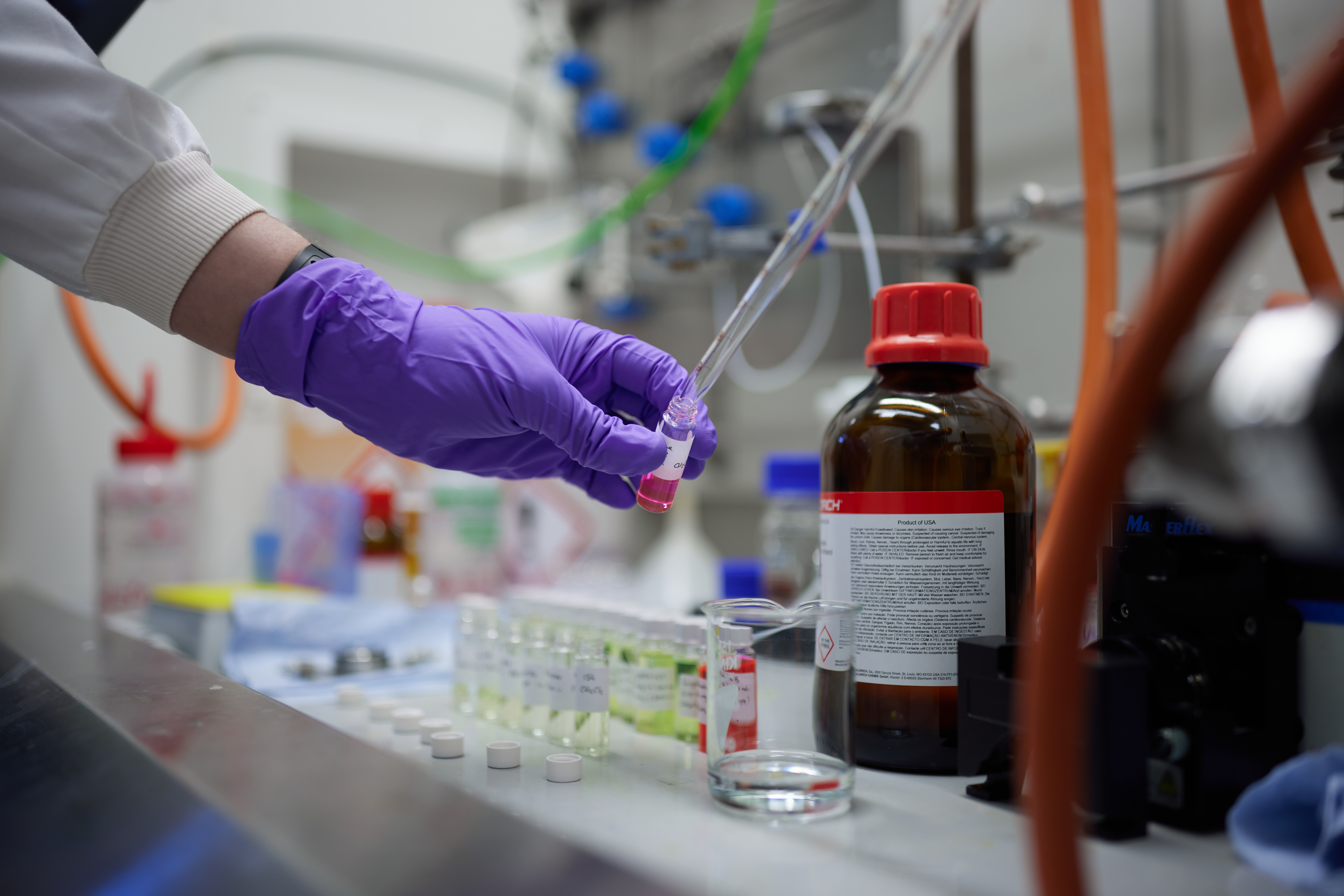 A gloved hand is picking up a vial of solution. in the background are more vials lined up.